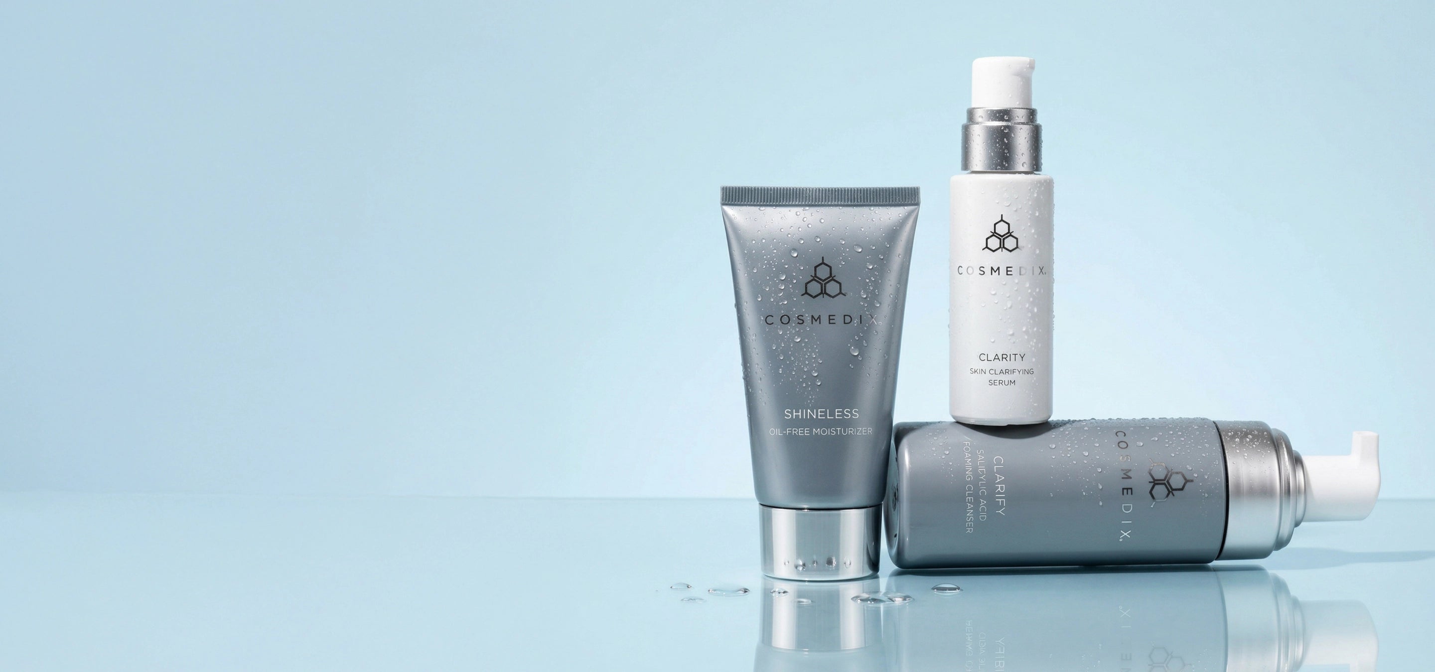 Shineless Moisturizer, Clarity Serum, and Clarify Cleanser displayed against a light blue background on a reflective surface. BREAKOUTS, REWRITTEN. 15% OFF ACNE ESSENTIALS. Cleanse, correct, and rebalance breakout-prone skin with a complete routine designed for visible results and long-term skin health.