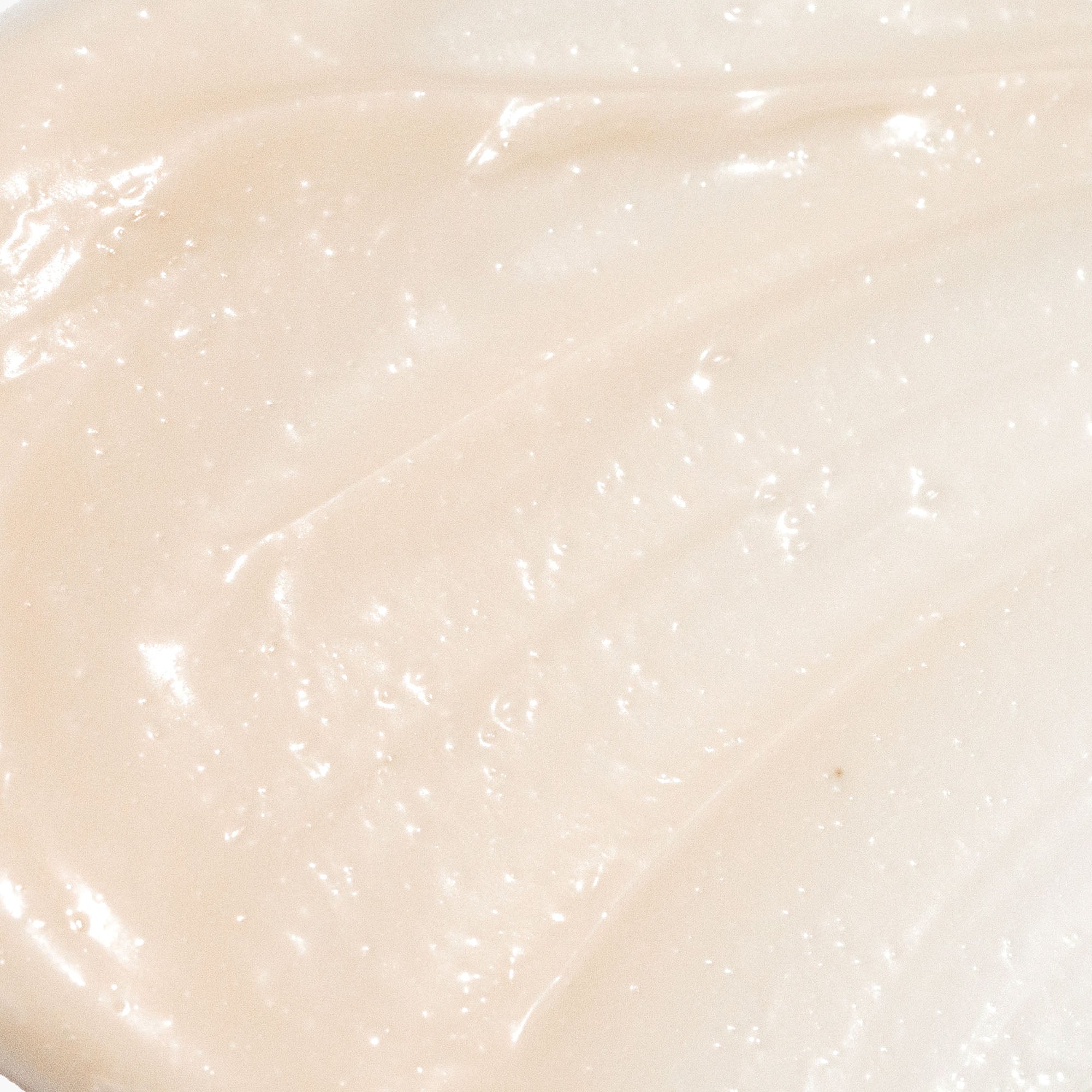 Angled Rescue Intense Hydrating Balm Mask tube beside a plate with two beige balm beads on a neutral gray background