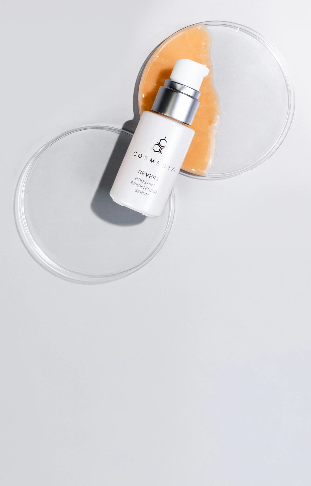 Revert Boosting Brightening Serum laying flat on table above petri dish with revert orange serum. 